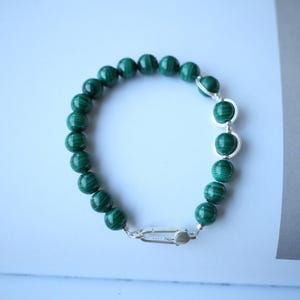 Op de afbeelding: Een groene malachiet kralen armband met een zilveren sluiting. De armband is gemaakt van ronde kralen en heeft een eenvoudig ontwerp.