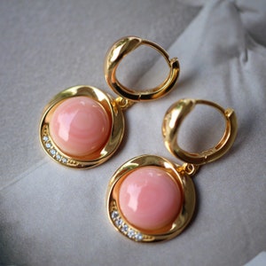 Può includere: Un paio di orecchini a cerchio dorati con pietre di corallo rosa e piccoli strass trasparenti.