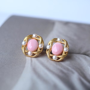 以下が含まれることがあります： ピンクの楕円形の石が小さな白い真珠で囲まれた、金色のイヤリングのペアです