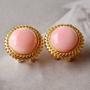 Può includere: Un paio di orecchini a clip dorati con cabochon di conchiglia rosa.