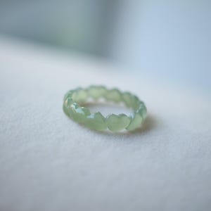 May include: A pale green jade ring with a unique design of interlocking heart shapes.