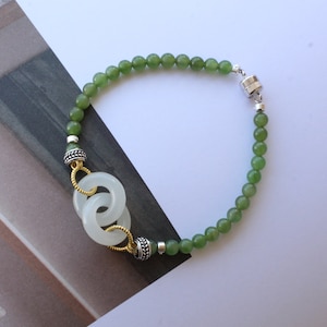 Può includere: Un braccialetto di perline di giada verde con una chiusura magnetica argentata e un ciondolo di giada bianca con accenti dorati.