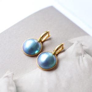 May include: A pair of gold hoop earrings with a blue pearl drop. The pearls are round and have a slight iridescent sheen.