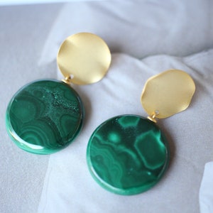 Puede incluir: Un par de pendientes de declaración dorados y verdes. Cada pendiente presenta una piedra redonda de malaquita verde y un disco dorado.