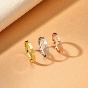 May include: Three minimalist rings in gold, silver, and rose gold. Each ring has a faceted design, creating a geometric look. The rings are displayed on a peach-coloured surface, with a soft, neutral background.