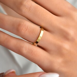 May include: A close-up of a gold ring with a geometric design. The ring is on a finger, and the gold colour is bright and shiny. The ring's surface is faceted, creating a textured appearance. The ring is a simple band style.