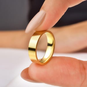 May include: A gold wedding band with a smooth, polished finish. The band is thick and has a classic design.
