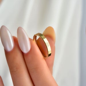 May include: A gold ring with a geometric, faceted design. The ring is held between fingers, showcasing its polished surface and intricate pattern. The ring's band is a continuous loop, reflecting light.