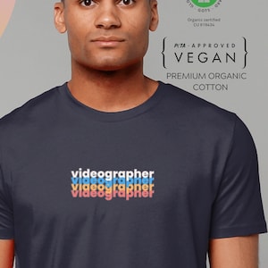 Könnte beinhalten: Ein marineblaues T-Shirt mit dem Text "videographer" in einem Regenbogen-Farbverlauf auf der Vorderseite. Das Shirt ist aus Bio-Baumwolle und vegan zertifiziert.