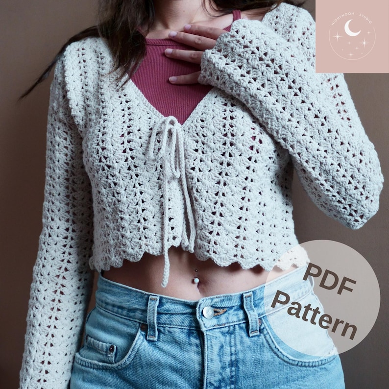 May include: A crochet cardigan with a tie front and long sleeves. The cardigan is a light beige color and has a delicate crochet pattern. The cardigan is cropped and has a scalloped hem.