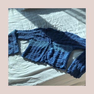 May include: A blue crocheted cardigan with a tie front and bell sleeves. The cardigan is made of a soft, lightweight yarn and has a relaxed fit.