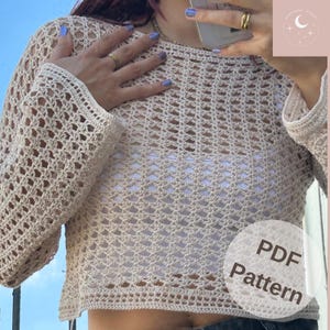 May include: A beige crochet top with long sleeves and an open weave. The top is cropped, revealing a white undershirt. The image includes a circular graphic with the text "PDF Pattern".