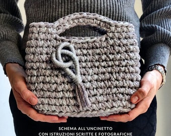 May include: A crocheted handbag in a light gray color with a silver tassel. The bag has a crocheted handle and a silver charm.