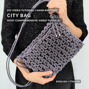 May include: A gray, hand-knitted City Bag with a drawstring closure and long strap. The bag is made with a looped stitch pattern. The image includes text that reads "DIY VIDEO TUTORIAL | HAND KNITTING", "CITY BAG", and "MOST COMPREHENSIVE VIDEO TUTORIAL".