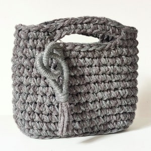 May include: A gray crocheted tote bag with a silver glitter finish and a silver tassel. The bag has a single handle and a silver key chain.