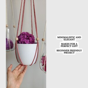 May include: A pink macrame plant hanger with wooden beads holds a white planter with pink flowers. The text "MINIMALISTIC AND ELEGANT MAKES FOR A PERFECT GIFT BEGINNER FRIENDLY PROJECT" is on a white sticker.
