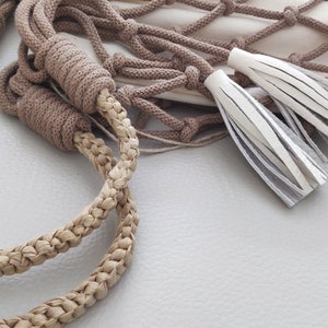 May include: Close-up of a brown rope with a braided texture. The rope is tied to a white mesh bag with two white leather tassels.