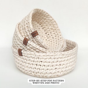 May include: Three crocheted baskets in various sizes, all in a cream color, with brown leather labels that say "A Mano".