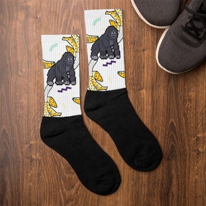 Könnte beinhalten: Ein Paar schwarze Socken mit einem weißen Design, das einen Gorilla und Bananen zeigt. Das Design ist im Pixel-Stil gehalten.