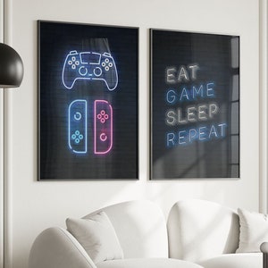 May include: Two black framed neon signs with white backgrounds. The left sign features a blue and pink neon video game controller and a Nintendo Switch console. The right sign features the text "EAT GAME SLEEP REPEAT" in blue neon.