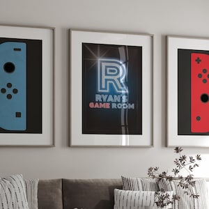 Puede incluir: Tres impresiones enmarcadas con un tema de juegos. La impresión de la izquierda presenta un mando Nintendo Switch Joy-Con azul, la impresión del medio presenta una letra R azul neón con el texto "Ryan's Game Room", y la impresión de la derecha presenta un mando Nintendo Switch Joy-Con rojo.