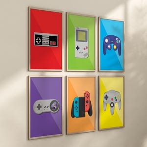 Puede incluir: Un conjunto de seis impresiones enmarcadas que presentan mandos y consolas de videojuegos retro. Las impresiones están sobre fondos coloridos, incluyendo rojo, verde, azul, morado, naranja y amarillo. Los mandos incluyen un mando de Nintendo Entertainment System, una Game Boy, un mando de GameCube, un mando de Super Nintendo, un mando de Nintendo Switch y un mando de Nintendo 64.