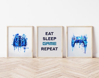 Könnte beinhalten: Drei gerahmte Drucke mit Bildern im Aquarellstil. Zwei Drucke zeigen blaue Gamecontroller mit Farbspritzereffekten. Der mittlere Druck hat den Text "EAT SLEEP GAME REPEAT" in Marineblau und Blaugrün.