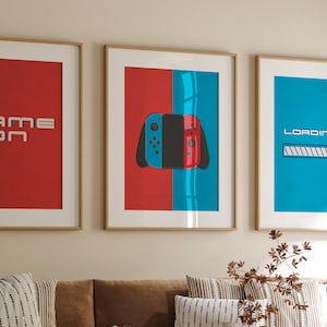 Può includere: Tre stampe incorniciate con un tema di gioco. La stampa a sinistra è rossa con il testo "GAME ON". La stampa centrale è divisa a metà, con il rosso a sinistra e il blu a destra. Al centro è mostrato un controller Nintendo Switch. La stampa a destra è blu con il testo "LOADING..." e una barra di avanzamento.