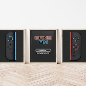 May include: Three framed prints with a gaming theme. The center print has the text "GAME ON" in red and blue neon lettering with a loading bar underneath. The left and right prints feature a black and white illustration of a video game controller with blue and red accents.