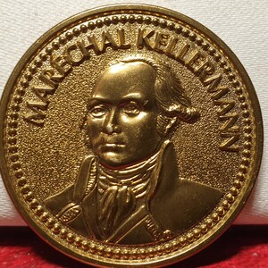 Op de afbeelding: Een gouden metalen munt met een portret van een man in militair uniform. De tekst "MARÉCHAL KELLERMANN" is rond de rand van de munt gegraveerd.