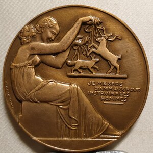 May include: A bronze medal with a woman holding a branch with animals on it. The text on the medal reads "JE ME SERS D'ANIMAUX POUR INSTRUIRE LES HOMMES".