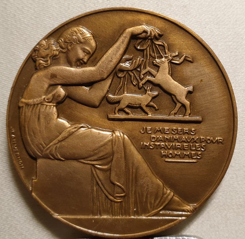 May include: A bronze medal with a woman holding a branch with animals on it. The text on the medal reads "JE ME SERS D'ANIMAUX POUR INSTRUIRE LES HOMMES".