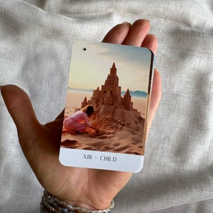 May include: A tarot card with a sandcastle and a child building it on a beach. The card is titled "XIII - CHILD".