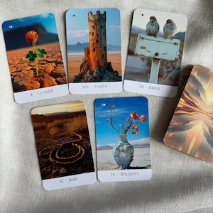 May include: Five tarot cards with different images and names. The cards are on a light beige fabric background. The cards are: II - Clover, XIX - Tower, XII - Birds, XI - Whip, IX - Bouquet.