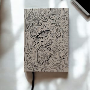 Può includere: Un quaderno beige con un'illustrazione in bianco e nero di un occhio stilizzato con linee e vortici astratti. Il quaderno ha un segnalibro a nastro nero.