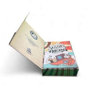May include: A Sailor's Arcana guide book in a decorative box. The box is open, revealing the book's cover with a cartoon illustration of a boat and the title "Sailor's Arcana". The box has a green and brown striped pattern.