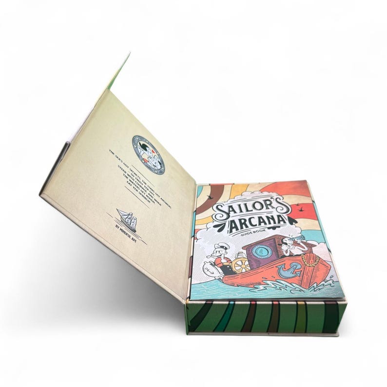 May include: A Sailor's Arcana guide book in a decorative box. The box is open, revealing the book's cover with a cartoon illustration of a boat and the title "Sailor's Arcana". The box has a green and brown striped pattern.