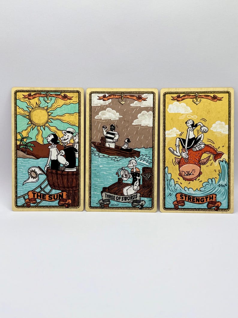 May include: Three tarot cards featuring cartoon characters. "The Sun" card shows a sunny beach scene. "Three of Swords" depicts a boat in the rain. "Strength" shows a character riding a fish. Each card has a decorative border and banner.