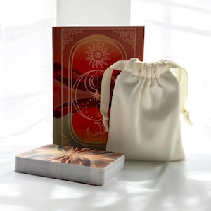 May include: A deck of tarot cards with a celestial design on the box and a white drawstring bag. The cards feature a variety of images, including a sun, moon, and stars.