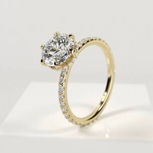 May include: A yellow gold ring featuring a large, round, brilliant-cut center stone held by six prongs. The slender band is adorned with a pavé setting of small, clear, round-cut stones that extend halfway around the circumference of the ring.