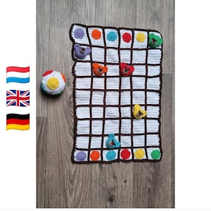 Puede incluir: Una manta rectangular de ganchillo blanca con un patrón de cuadrícula marrón oscuro y detalles circulares coloridos. Varias cabezas de oso de ganchillo tridimensionales en varios colores están unidas a la cuadrícula. Se incluye una pelota de ganchillo redonda a juego.