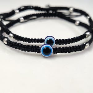 Op de afbeelding: Twee zwarte armbandjes van koord met zilveren kralen en blauwe boze oog bedels.