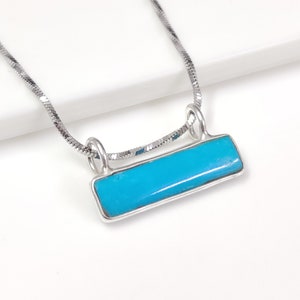 Könnte beinhalten: Eine silberne Kettenkette mit einem Anhänger aus Türkis. Der Anhänger ist rechteckig und hat eine glatte, polierte Oberfläche.