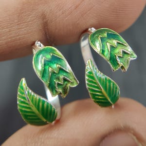 Op de afbeelding: Een paar zilveren ringen met groene emaille bladeren en bloemen. De ringen zijn ontworpen om aan de vinger te worden gedragen.