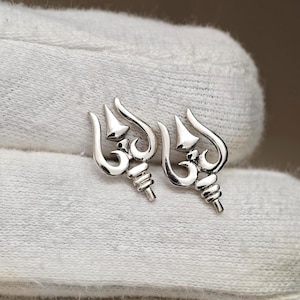 May include: A pair of polished silver-toned stud earrings shaped like a trident with a central pointed tip and curved side prongs. The design features a small horizontal bar and a ribbed base section, creating a symmetrical metallic emblem.