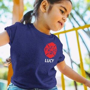 Young girl at playground wearing a navy blue t-shirt with red Maltese cross and her name Lucy underneath.