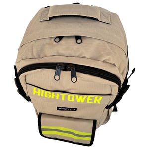 K&ouml;nnte beinhalten: Beigefarbener Rucksack mit schwarzen Rei&szlig;verschl&uuml;ssen und einem oberen Griff. Das Wort "HIGHTOWER" ist in leuchtendem Gelb auf der Vorderseite aufgedruckt. Eine kleine Tasche mit reflektierenden Streifen ist unten sichtbar.