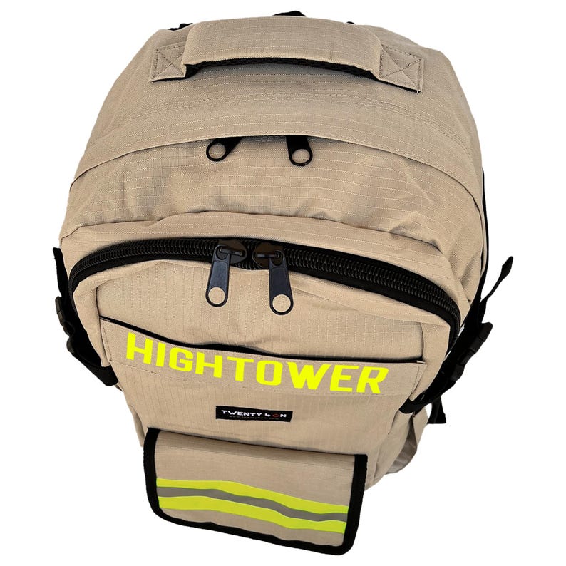 K&ouml;nnte beinhalten: Beigefarbener Rucksack mit schwarzen Rei&szlig;verschl&uuml;ssen und einem oberen Griff. Das Wort "HIGHTOWER" ist in leuchtendem Gelb auf der Vorderseite aufgedruckt. Eine kleine Tasche mit reflektierenden Streifen ist unten sichtbar.