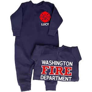 Puede incluir: Dos monos de bebé azul marino. Uno tiene un emblema de bombero rojo con el nombre "LUCY" en blanco. El otro tiene las palabras "WASHINGTON FIRE DEPARTMENT" en blanco y rojo.