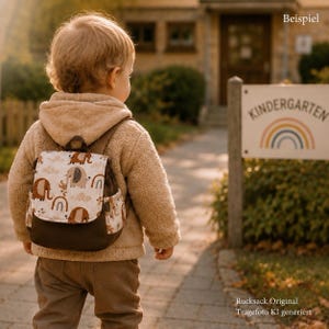 Könnte beinhalten: Ein kleiner Rucksack mit einer cremefarbenen Klappe, die mit einem sich wiederholenden Muster aus braunen Elefanten, Regenbögen und Wolken bedruckt ist. Der Hauptteil des Rucksacks besteht aus einfarbigem, dunkelbraunem Stoff mit verstellbaren Trägern.